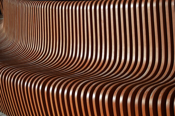 Wooden brown curved slats. Beautiful reflections of the sun on the surface of the bench element....
