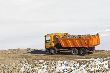 Obraz premium Industrial dump truck with trailer loaded with stones and rubble on road building construction site covered with snow in winter on Zlatibor mountain in Serbia