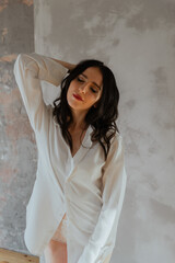 Sexy young brunette girl in a white shirt and lingerie in a loft photo studio