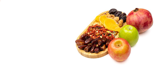 Festive white background with pomegranate and apples, fruits on a wooden tray, dates, nuts, dried mango, prunes