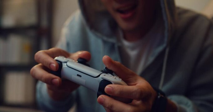 Close-up Happy young Asian man wear gray hoodie hold joystick controller excitement and shouting while having fun winning playing video game sit on sofa in the living room home at night.