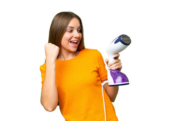 Young blonde woman holding a vertical steam iron over isolated chroma key background celebrating a victory
