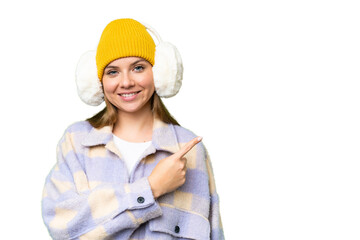 Young blonde woman wearing winter muffs over isolated chroma key background pointing to the side to present a product