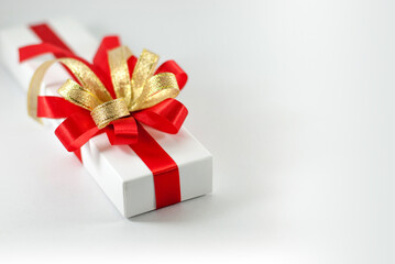 White gift box with red and gold ribbon on a white background with copy space on the right.