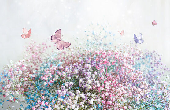 Beautiful gentle spring light background image in pink pastel colors with fluffy small flowers and a group of butterflies fluttering over flowers.