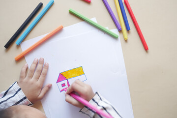 top view of child girl drawing a house with color pencils on paper 