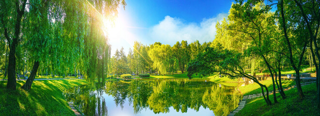 Very beautiful idyllic natural panorama of city spring summer park with pond that reflects surrounding trees and blue sky on bright sunny day.