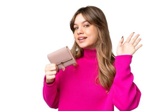 Young girl holding a wallet over isolated chroma key background saluting with hand with happy expression