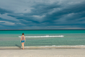 Obraz premium Woman walking along San Teodoro sand beach with turquoise sea water in Sadinia Italy, clouds in the sky during summer