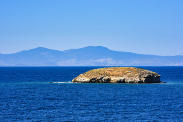 Fototapeta premium A Small islet, cliffs, mountain and bay view in the virgin bays of İzmir Foça. Virgin coves of the Aegean Sea. Phokaia, Izmir Bays.The view of the Karaburun mountains and the Aegean Gulf from Foça.