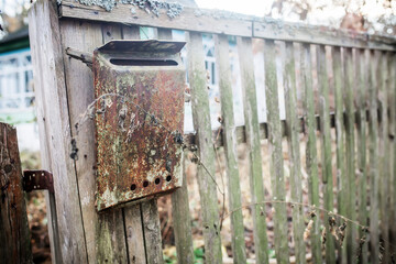 An old mailbox on the fence. Vintage rusty mailbox on a wooden fence near the gate of an abandoned house. The abandoned house of Ukrainians. Life of migrant migrants.