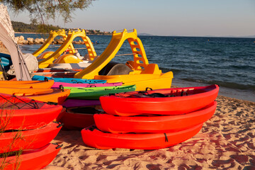 Multi-colored kayaks and pedalos for rental on a sandy beach. Tourist entertainment.