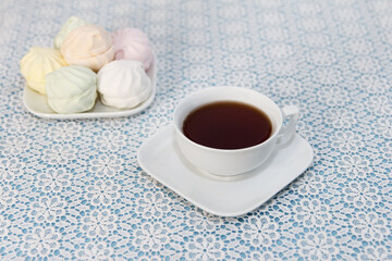Traditional delicious brewed tea in a cup and air marshmallows lie on table, a sweet dessert