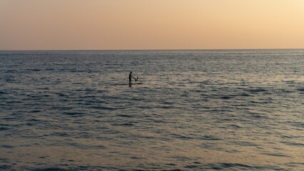 Fototapeta premium person on surfboard in the middle of the sea at sunset in huatulco beach oaxaca, mexico