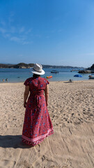 Beautiful woman in pink dress walking on the sand of the blue sea in huatulco oaxaca, mexico
