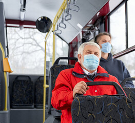 Fototapeta na wymiar Passengers protecting by medical masks traveling by public transpost, sitting on bus. People going by bus home, old man and brunette man sitting, looking. Concept of pandemic.
