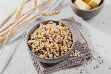 Bowl of cooked peeled barley grains porridge with ears of wheat on white background. Cooking Healthy and diet food concept.