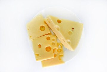 A large piece of cheese with holes on the plate. Chopped cheese and small slices on a white background. Juicy and delicious natural cheese. Cheese holes.