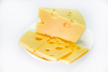 A large piece of cheese with holes on the plate. Chopped cheese and small slices on a white background. Juicy and delicious natural cheese. Cheese holes.