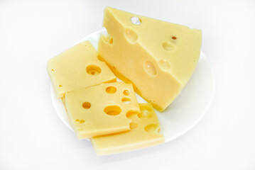 A large piece of cheese with holes on the plate. Chopped cheese and small slices on a white background. Juicy and delicious natural cheese. Cheese holes.