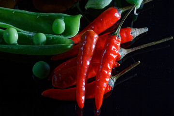 colorful green peas and different chilli at a wooden plate and black background