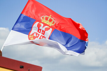 The flag of serbia against the blue sky flutters in the wind. Flag of a country in Europe.