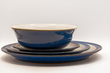 a centred bowl and three sizes of crockery plates in white with blue rims and edges and a gold trim