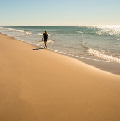 Jeune femme marchant le long de la plage les pieds dans la mer.