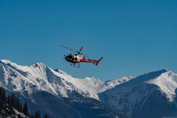 Fotobehang A helicopter taken in flight in front of a snowy mountain panorama © Stan Weyler