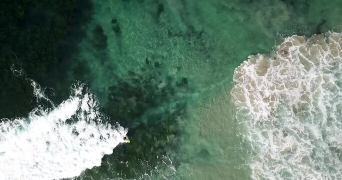 A solitary surfer catches a wave in aerial view of abstract emerald and aqua toned sea 