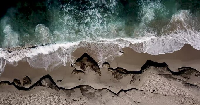 Aerial top down motion pan over a secluded sandy Southern California beach with waves crashing