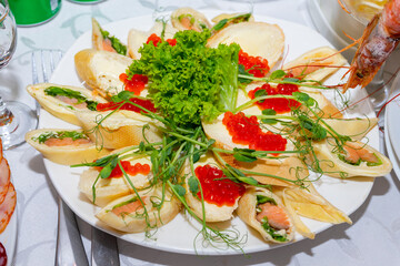 Pancakes with red fish and red caviar are decorated with greens. Cold snacks on the festive table
