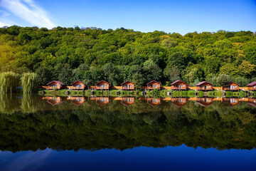 Fototapeta na wymiar Wooden houses on the water near the forest for carp fishing. A place to relax in nature. Spring carp fishing season.
