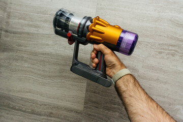 Male hand holding POV new cordless vacuum cleaner with empty bin readt to vaccum multiple dust particle, hair and other debris found in house