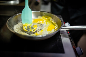 man chef cooking scrambled eggs in frying pan on kitchen