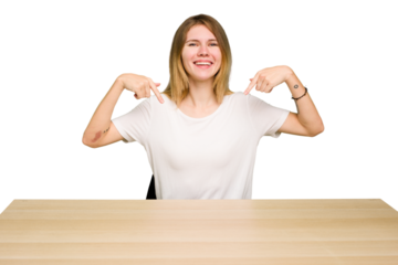 Young caucasian woman sitting on a chair in a desktop isolated points down with fingers, positive feeling.