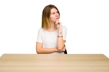 Young caucasian woman sitting on a chair in a desktop isolated looking sideways with doubtful and skeptical expression.