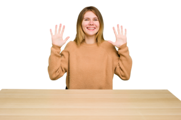 Young caucasian woman sitting on a chair in a desktop isolated showing number ten with hands.