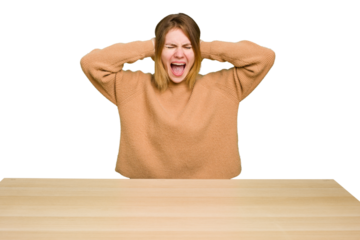 Young caucasian woman sitting on a chair in a desktop isolated covering ears with hands trying not to hear too loud sound.
