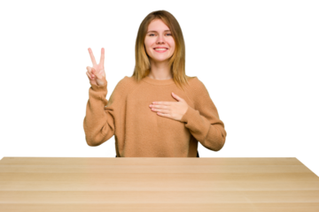 Young caucasian woman sitting on a chair in a desktop isolated taking an oath, putting hand on chest.