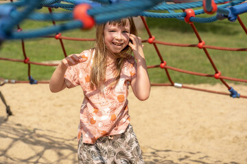 One happy elementary school age child cheerful girl smiling, laughing on a playground looking at camera, portrait, generic modern trendy clothes. Playing outdoors, true happiness, leisure, recreation
