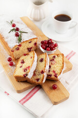 On a light table, a cupcake with cranberries on a wooden board and a cup of coffee in the background.