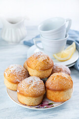 Blurred image of tender muffins on a plate and tea cups on a light table.