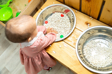 Top down view of toddler playing sensory game with dried pits and nuts