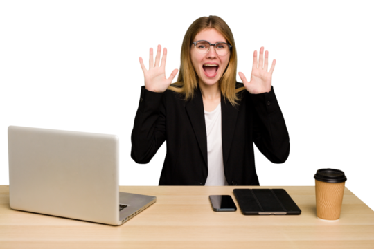 Young business caucasian woman working on her workplace cutout isolated receiving a pleasant surprise, excited and raising hands.