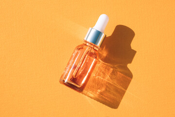 Natural face beauty oil with vitamin C. Glass dropper bottle with face serum over orange background with shadows, beauty skin-care products with natural ingredients and fruit essence. Mockup image