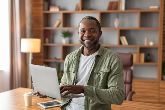 Smiling attractive mature black male manager with laptop work, make presentation and look at camera