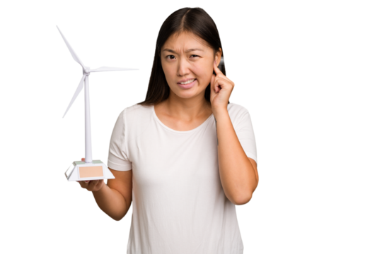 Young asian woman holding a small wind energy mill isolated covering ears with hands.