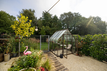 Morning view on backyard with beautiful vintage greenhouse. Tiny and cozy garden near forest