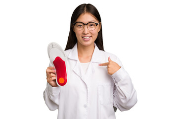 Young asian chiropodist holding a insoles for shoes isolated person pointing by hand to a shirt copy space, proud and confident